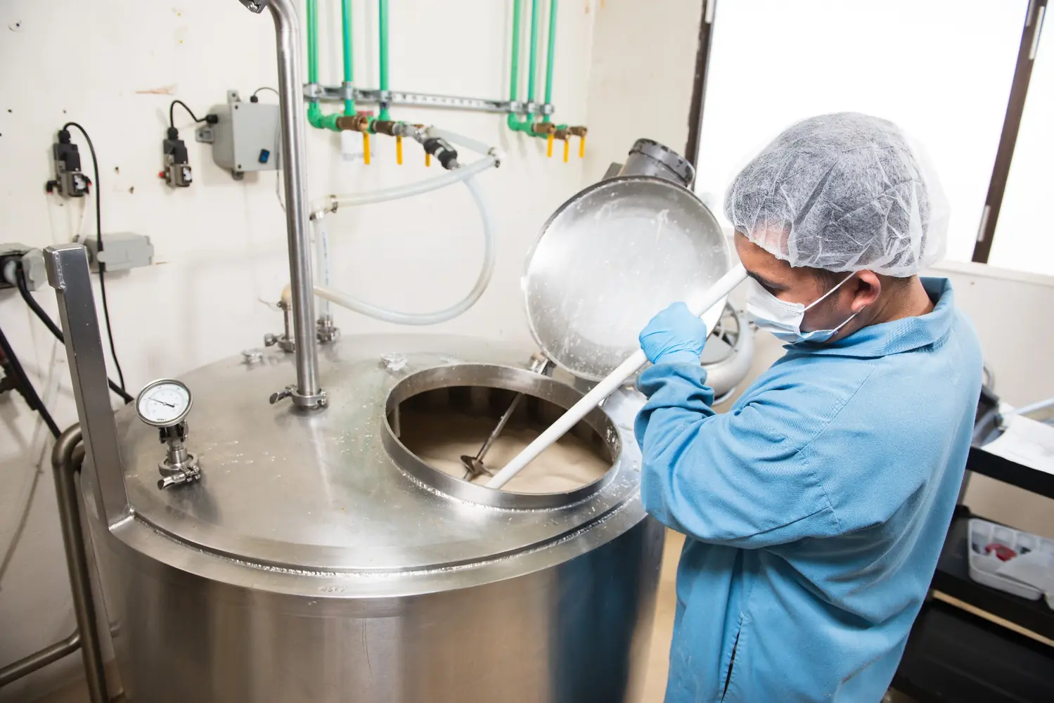 An operator adding ingredients to a stainless-steel kettle