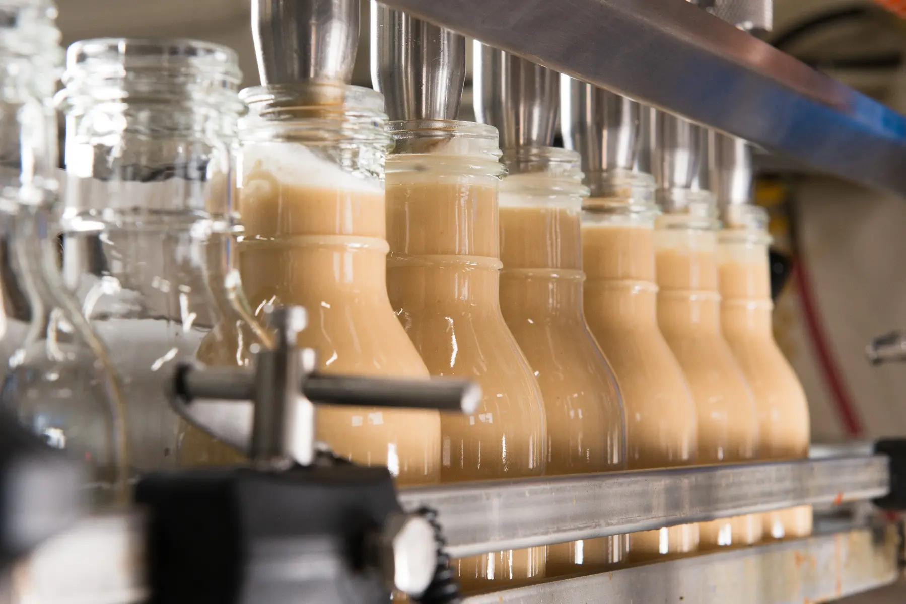Evenly filled, unlabelled sauce bottles on the Just Perfect Specialty Foods filling line